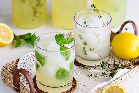 Two glasses of homemade lemonade on a tray with mint and thyme garnish